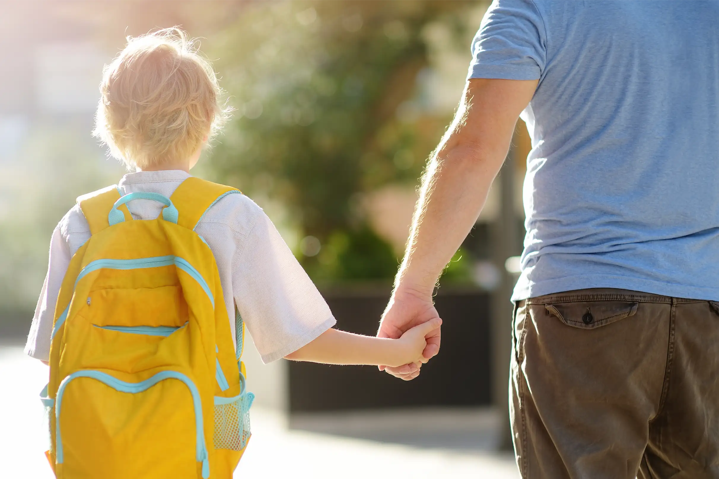 Ein Mitarbeiter in Zivilerkleidung begleitet ein Kind zur Schule